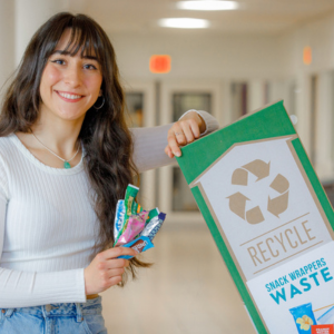 Woman holding snack wappers and leaning against a green box